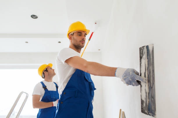 business, building, teamwork and people concept - group of builders in hardhats with plastering tools indoors