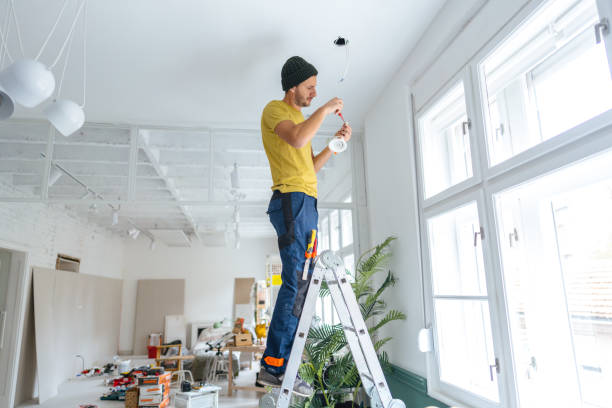 Photo of a young electrician fixing and changing ceiling lights, using a screwdriver.